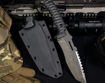Può includere: Un coltello a lama fissa con impugnatura nera testurizzata e lama dal finish scuro e usurato con dorso seghettato. Il coltello è accompagnato da un fodero nero sagomato con occhielli metallici, posizionato accanto a equipaggiamento tattico e un fucile.
