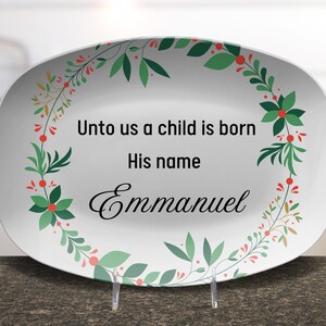 Könnte beinhalten: Weiße ovale Servierplatte mit einem grünen und roten floralen Kranzrand. Der Text "Unto us a child is born His name Emmanuel" ist in Schwarz innerhalb des Kranzes gedruckt.