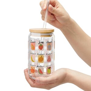 Puede incluir: Una botella de agua reutilizable de vidrio transparente con tapa de bambú y una pajita. La botella tiene un diseño colorido con ilustraciones de frutas y las palabras "Amor, Alegría, Paz, Paciencia, Bondad, Benevolencia, Fidelidad, Suavidad, Autocontrol".