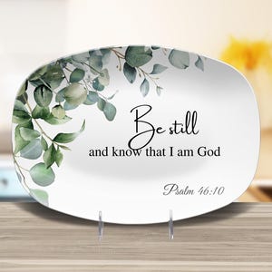 May include: White oval serving platter with a green watercolor eucalyptus leaf design. The platter has the text "Be still and know that I am God" and "Psalm 46:10" printed on it.