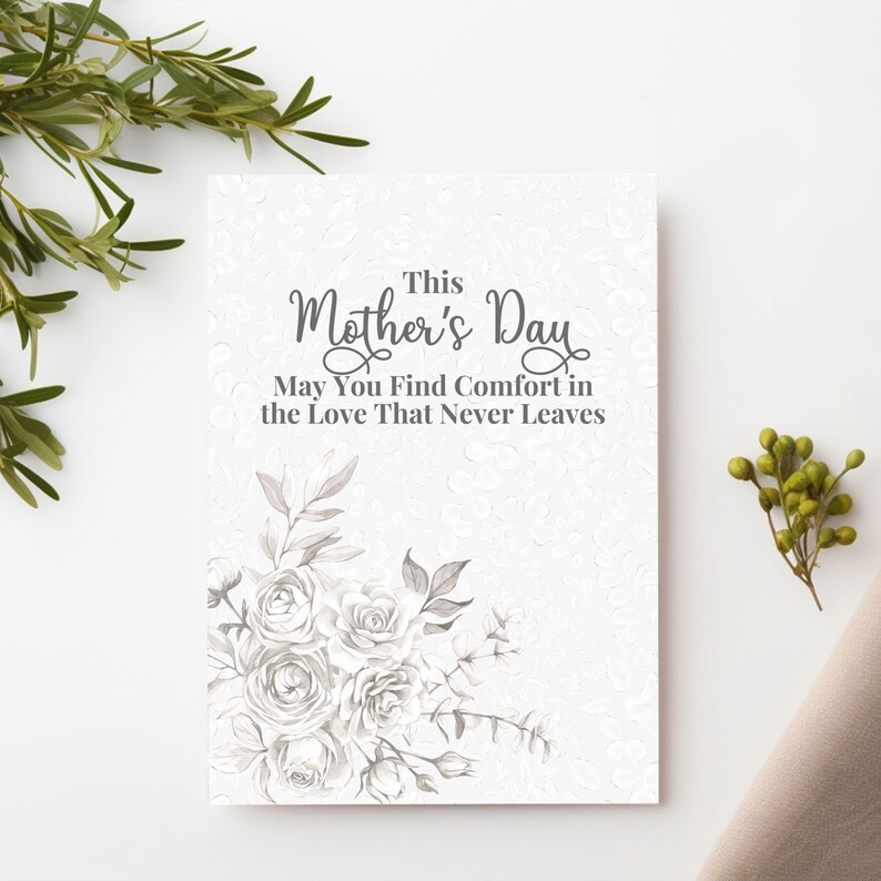Puede incluir: Una tarjeta blanca del D&iacute;a de la Madre con ilustraciones florales y el texto "This Mother's Day, May You Find Comfort in the Love That Never Leaves." La tarjeta presenta un fondo texturizado y est&aacute; decorada con rosas y hojas grises.