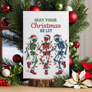 May include: A Christmas card with the text "MAY YOUR Christmas BE LIT". The card features three dancing skeletons wearing Santa hats and wrapped in Christmas lights. The card is surrounded by Christmas decorations.