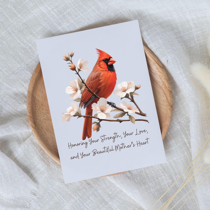 Puede incluir: Un p&aacute;jaro cardenal rojo posado en una rama con flores blancas. El texto dice "Honoring Your Strength, Your Love, and Your Beautiful Mother's Heart."