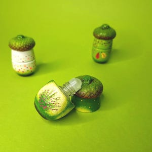 May include: Three small acorn-shaped bottles with green and brown painted details. One bottle is open and shows a clear glass rollerball inside.
