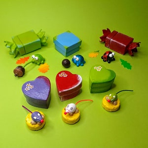 May include: A collection of small, hand-painted wooden boxes in various shapes and colours, including a heart, a square, and a candy shape. There are also small figurines of a ladybug, a frog, and a mouse.