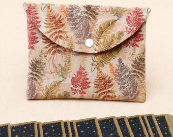 May include: A rectangular fabric pouch featuring a beige background with a repeating pattern of fern leaves in shades of red, orange, and brown. The pouch has a triangular flap secured by a single white snap button. Below it are several dark blue rectangular cards with gold star patterns.