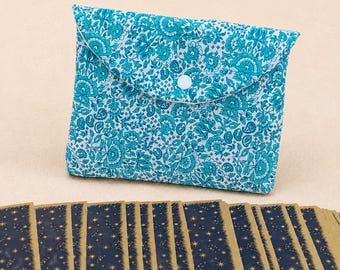 May include: A teal and white floral patterned fabric pouch with a single white snap closure, positioned behind a horizontal row of rectangular cards featuring a dark blue night sky design with gold stars and a gold border on each card.