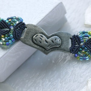 May include: A blue and green beaded bracelet with a silver heart charm. The heart charm has a small rhinestone in the center.