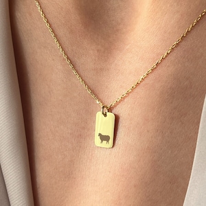 Könnte beinhalten: Eine goldene Kettenkette mit einem rechteckigen Anhänger, der eine Silhouette eines Schafes zeigt.