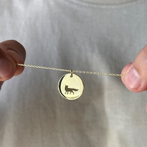 May include: A gold chain necklace with a round pendant featuring a silhouette of a fox.