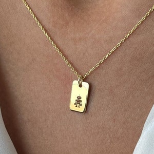 May include: A gold chain necklace with a small rectangular pendant featuring a robot design.