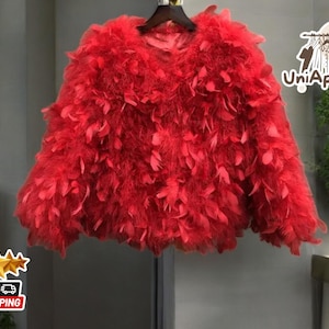 Könnte beinhalten: Eine rote Federjacke mit flauschiger Textur. Die Jacke hat einen runden Ausschnitt und lange Ärmel.