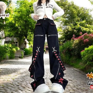 Könnte beinhalten: Schwarze Hose mit rosa Stern-Akzenten und verstellbaren Trägern. Die Hose hat eine lockere Passform und ist aus strapazierfähigem Stoff gefertigt.