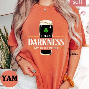 May include: Orange t-shirt with a graphic of a pint of dark beer with a shamrock and the words "Hello Darkness My Old Friend". The shirt has a "Bestseller" badge and "super soft" text.
