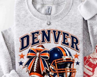 May include: A light gray crewneck sweatshirt featuring the word DENVER in dark blue letters with white outlines. Below the text is a brown football with a large orange and blue bow and a dark blue football helmet with orange and blue stripes.