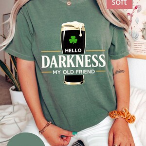 May include: Moss green t-shirt with a graphic of a pint of stout beer with a shamrock and the text "Hello Darkness My Old Friend". The shirt is labeled "Bestseller" and "Super Soft".