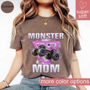 May include: Espresso-colored t-shirt with a graphic of a pink monster truck inside a pink triangle, with the words "MONSTER MOM" in silver. The shirt has a soft texture and offers more color options.