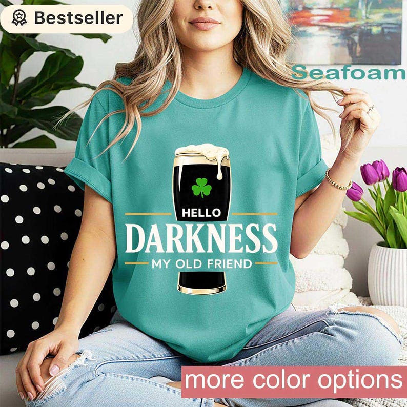 May include: Seafoam green t-shirt with a graphic of a pint of dark beer with a shamrock and the text "Hello Darkness My Old Friend". The shirt has rolled-up sleeves and is a bestseller.