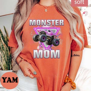 May include: Orange t-shirt with the text "MONSTER MOM" and a graphic of a purple monster truck. The shirt also has the text "super soft" and "more color options".