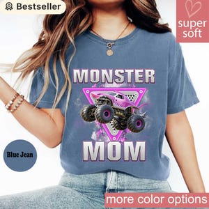 May include: Blue jean-colored t-shirt with the words "MONSTER MOM" and a graphic of a pink monster truck. The shirt has a crew neck and short sleeves. The shirt is labeled "Super Soft" and "Bestseller".