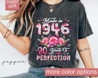 May include: A dark gray t-shirt with the text "Made in 1946" and "80 Years Of PERFECTION" in a floral design. The shirt has a vintage look and the words "super soft" and "more color options" are also visible.