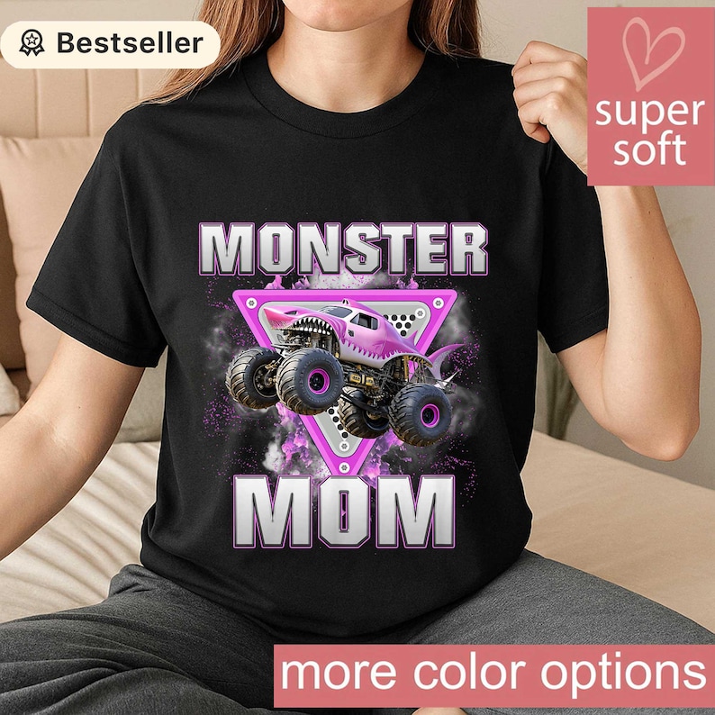 May include: Black t-shirt featuring a pink monster truck design with the words "MONSTER MOM" in white and pink. The truck is set against a purple and black background, with the words "more color options" at the bottom.