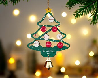 May include: A green wooden Christmas tree ornament with a star and bell. It features red and white circular ornaments with names, and the text "The Smith Family 2025". The ornament hangs from a twine string.