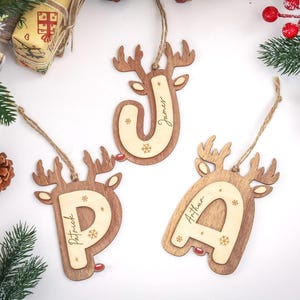 May include: Three wooden Christmas ornaments shaped like reindeer heads, each featuring a large letter P, J, or A in the center. The letters are engraved with names Patrick, James, and Arthur, and decorated with small snowflake icons.