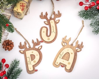 May include: Wooden Christmas ornaments shaped like reindeer with the letters "J", "P", and "A" cut out and personalized with names. Each ornament has a twine loop for hanging and snowflake details.