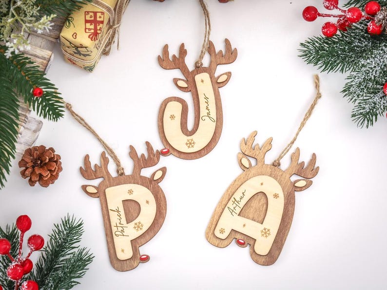 May include: Three wooden Christmas ornaments shaped like reindeer heads, each featuring a large letter P, J, or A in the center. The letters are engraved with names Patrick, James, and Arthur, and decorated with small snowflake icons.