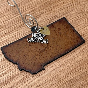 Peut inclure: Une décoration en métal brun en forme de l'état du Montana avec un charme argenté qui dit "Joyeux Noël" et un charme en forme de cœur doré avec l'année "2024" gravée dessus.