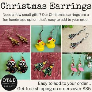 May include: A collection of six pairs of Christmas-themed dangle earrings featuring gold-tone and silver-tone metal hooks. Designs include yellow rubber ducks with Santa hats, black cats with holiday lights, pink flamingos, and various Christmas trees.