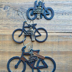 May include: Three dark metal bicycle ornaments with silver-toned wire hooks. Each bicycle features a dangling charm with the text Merry Christmas and a small rectangular metal tag engraved with the year 2026, suspended from the frame.