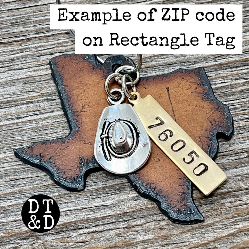 May include: A brown leather cutout in the shape of Texas with a silver-toned cowboy hat charm and a rectangular brass tag stamped with the number 76050. The charms are attached to a metal jump ring, creating a decorative accessory piece.