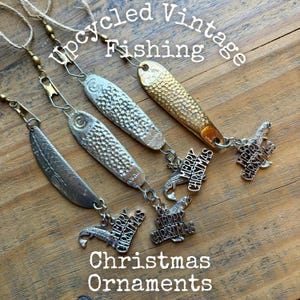 May include: Three upcycled vintage fishing lure ornaments with metallic finishes, including silver and gold tones. Each lure features a textured surface, a metal swivel, a twine loop, and a dangling silver charm with the text Merry Christmas.