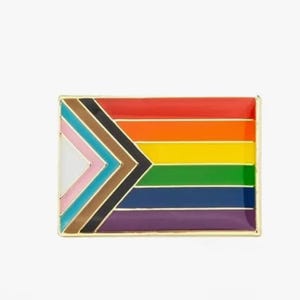 May include: A gold-coloured enamel pin featuring a rainbow flag with a black, brown, light blue, pink, and white chevron design on the left side.