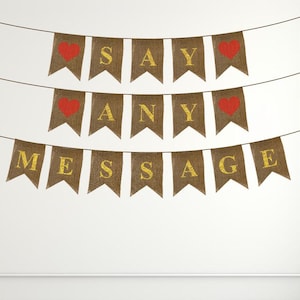 May include: A burlap banner with gold glitter letters that reads "SAY ANY MESSAGE" with red hearts on each end.