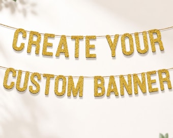 May include: A two-line banner featuring gold glitter letters strung on a thin cord. The top line spells out CREATE YOUR and the bottom line spells out CUSTOM BANNER. The letters are in a bold, sans-serif font with a sparkling, textured finish.