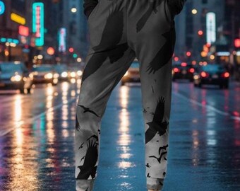 May include: A woman wearing a black cropped hoodie and gray sweatpants with a raven design. The sweatpants feature a gradient from dark gray to light gray, with black raven silhouettes. She is wearing white sneakers.