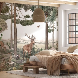 Puede incluir: Un dormitorio con un mural con temática de bosque que representa ciervos, árboles y otros animales del bosque. La habitación incluye una cama con ropa de cama beige, una mesita de noche de madera y una lámpara colgante tejida. Una planta en maceta está en la esquina.