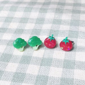 Peut inclure: Un ensemble de quatre boucles d'oreilles représentant des aliments miniatures. Deux boucles d'oreilles sont vertes et en forme de brocoli, et deux boucles d'oreilles sont rouges et en forme de fraises.