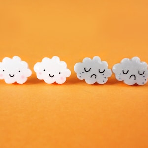 May include: Four white and grey cloud-shaped buttons with different facial expressions. Two clouds are smiling, and two clouds are frowning with teardrops.