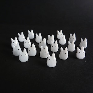 May include: A collection of 17 white ceramic figurines shaped like rabbits. The figurines are all facing forward and have a simple, minimalist design.