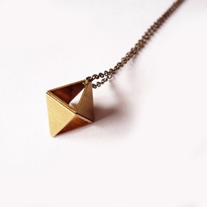May include: A gold necklace with a geometric pendant shaped like a pyramid. The pendant is hollow and has a textured surface.