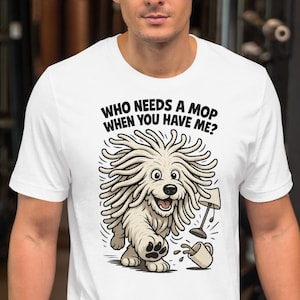 May include: White t-shirt with a cartoon dog design. The dog has dreadlocks and is holding a mop and a broken bucket. The text "WHO NEEDS A MOP WHEN YOU HAVE ME?" is printed above the dog. The shirt is worn by a person in a gym.