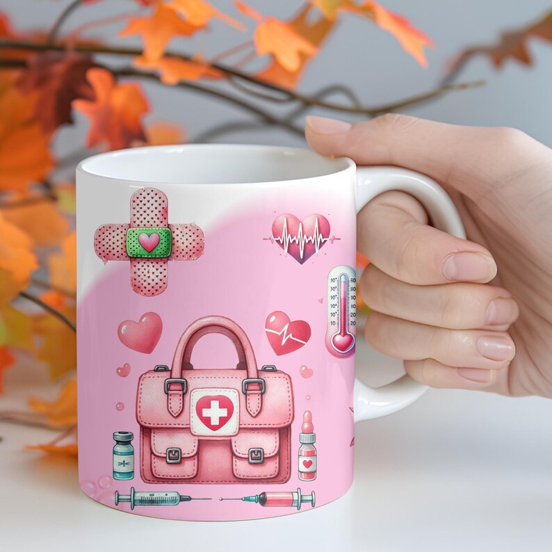Peut inclure: Mug en c&eacute;ramique blanche avec un th&egrave;me m&eacute;dical rose. Le motif comprend un sac de premiers secours rose, des c&oelig;urs, un pansement, un thermom&egrave;tre et des seringues. Le mug est tenu par une main, avec des feuilles d'automne en arri&egrave;re-plan.
