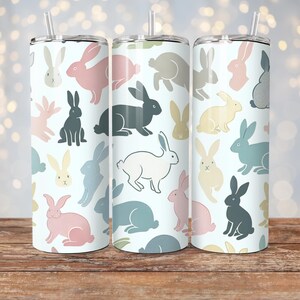 May include: Three stainless steel tumblers with a white background and a repeating pattern of colorful bunnies. The tumblers have lids and straws.