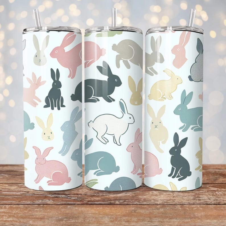 May include: Three stainless steel tumblers with a white background and a repeating pattern of colorful bunnies. The tumblers have lids and straws.