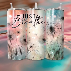 Op de afbeelding: Drie roestvrijstalen bekers met deksels en rietjes. Elke beker heeft een ander pastel kleurenschema en een paardenbloem ontwerp. De woorden "JUST Breathe" staan in een scriptletter op de voorkant van de bekers.