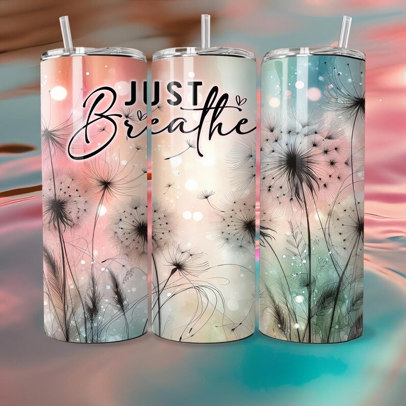 Op de afbeelding: Drie roestvrijstalen bekers met deksels en rietjes. Elke beker heeft een ander pastel kleurenschema en een paardenbloem ontwerp. De woorden "JUST Breathe" staan in een scriptletter op de voorkant van de bekers.